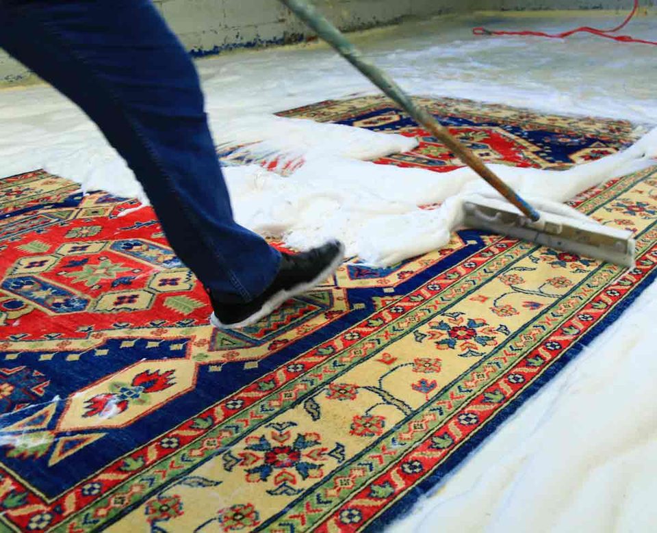 Hand-knotted rug covered in cleaning foam on a wash floor as a squeegee works the solution through the pile