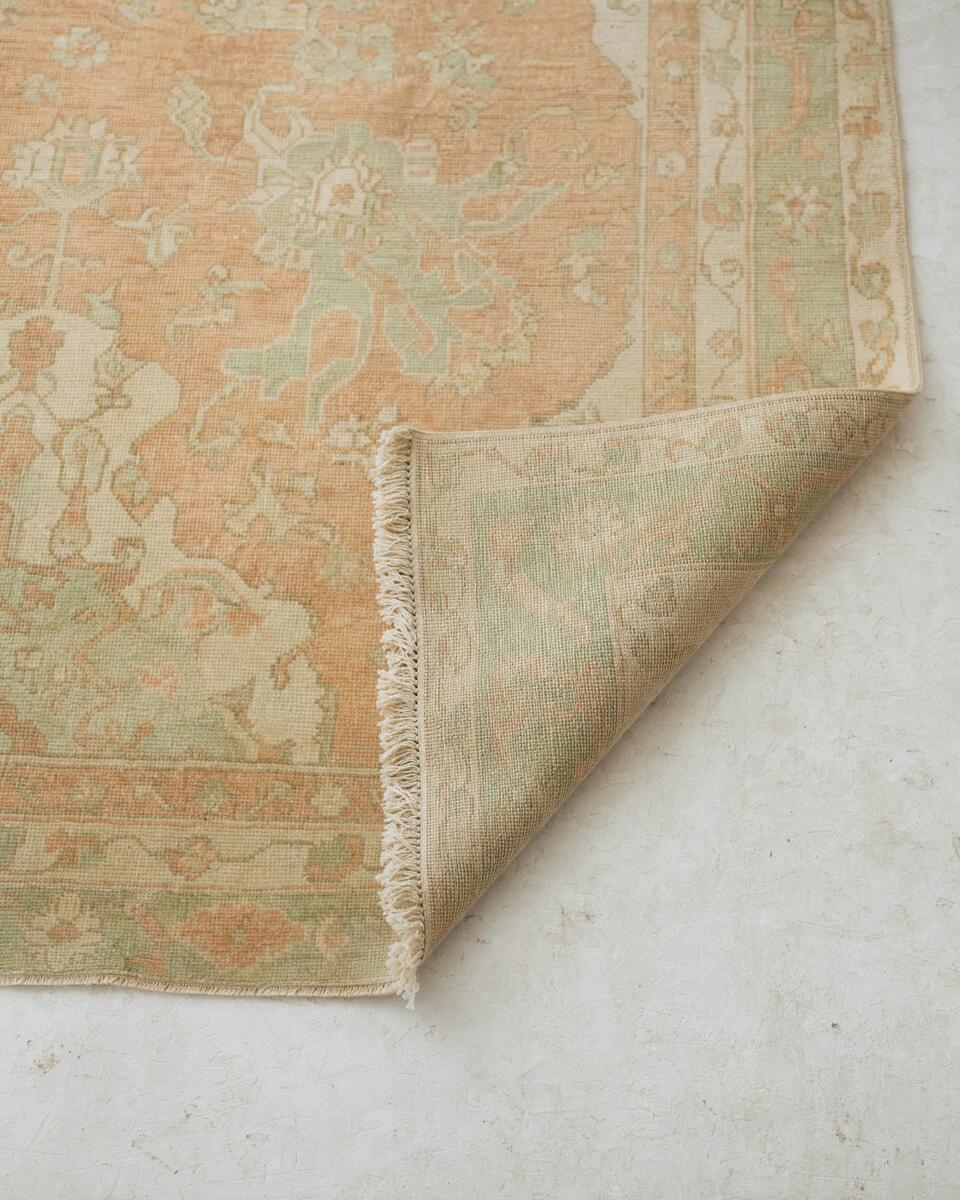 Vintage Turkish Oushak rug in apricot and sage with a folded corner showing the weave and fringe