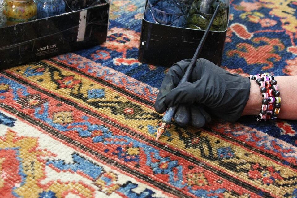 Restorer re-coloring worn areas of a rug border by hand with a fine dye pen