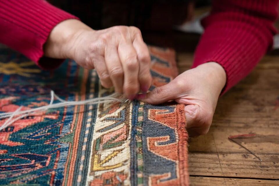 Restorer working new yarn into the end of a flatweave rug by hand
