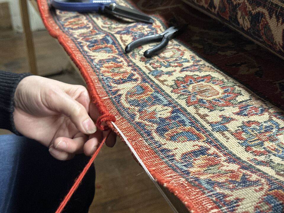 Overcasting the side edge of a Persian rug by hand with matched red wool