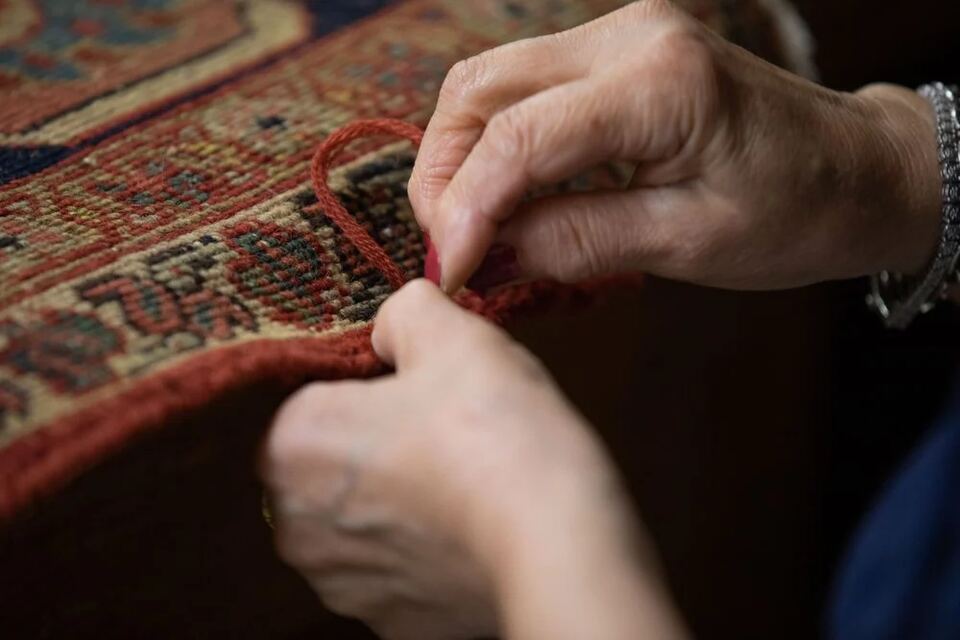 Hand-wrapping a rug's edge with red wool yarn during binding repair