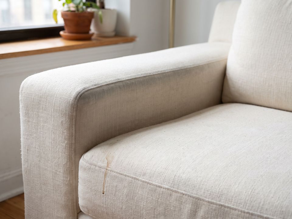 Illustration: cream linen sofa arm with body-oil soiling and a coffee drip before cleaning