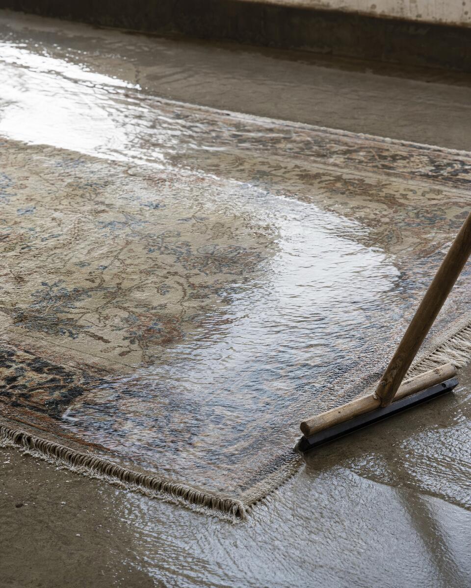 Water rinsing across the pile of a hand-knotted wool rug on a workshop wash floor
