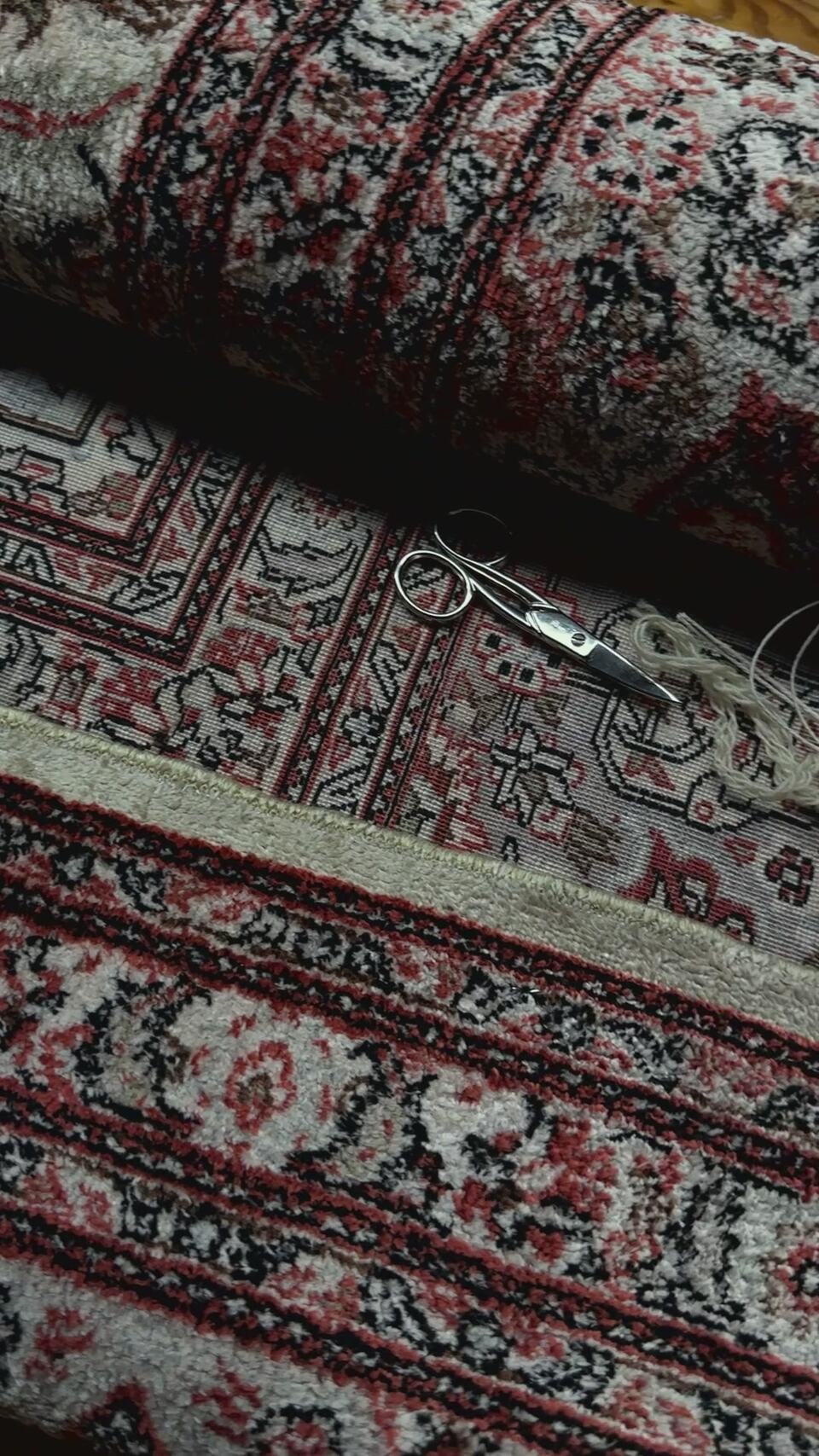 Hand-knotted Persian rugs rolled side by side in our Brooklyn workshop, with scissors and thread for finishing